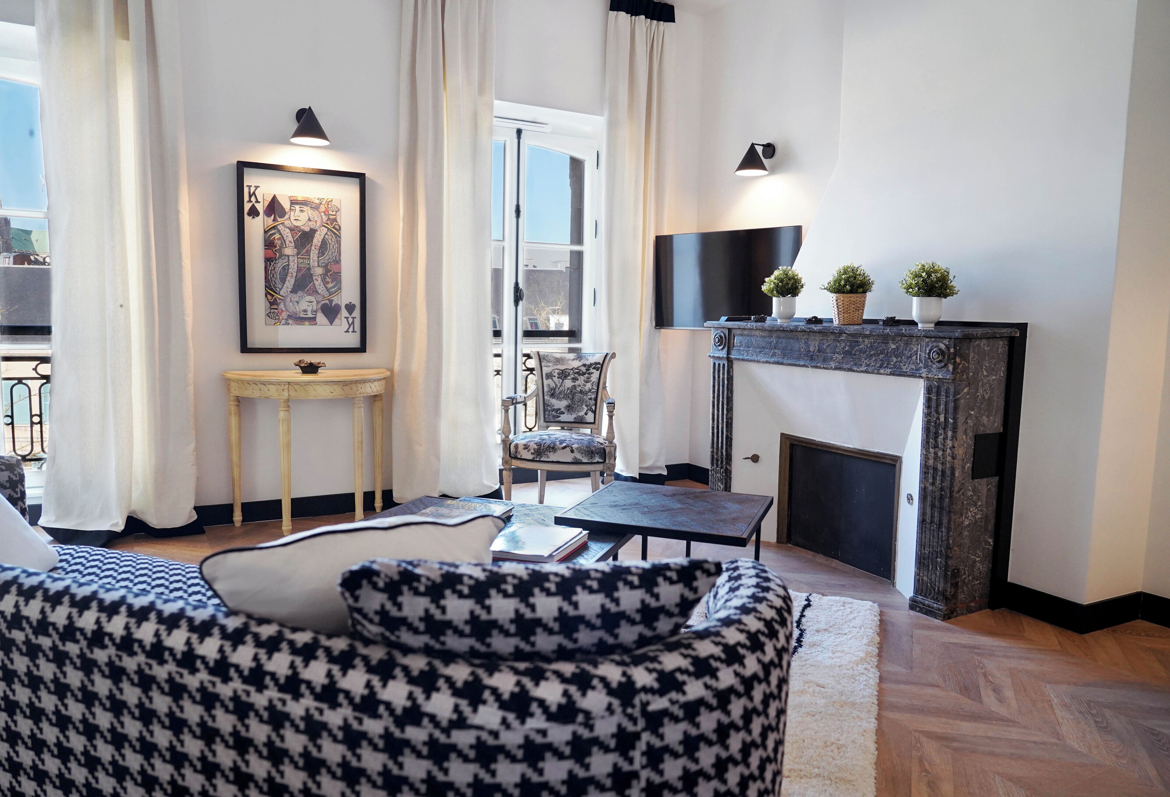 A living room with a houndstooth sofa, a small table with a book, a framed picture on the wall, and a fireplace with decorative items.
