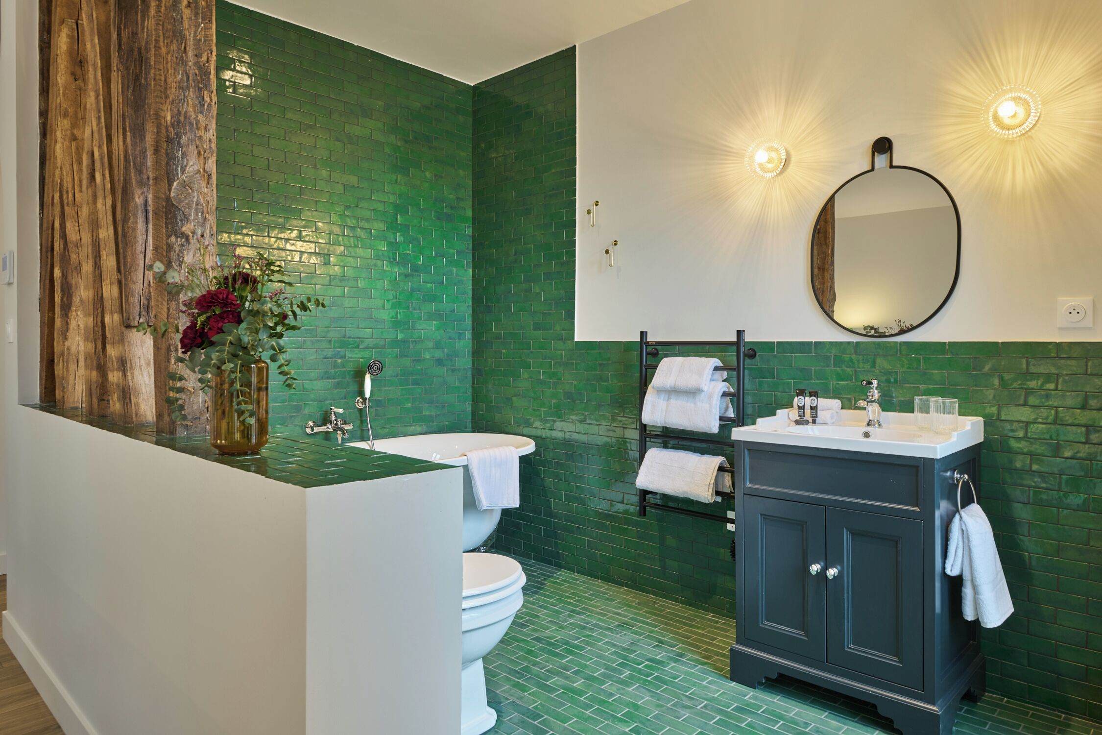Une salle de bain avec un mur recouvert de carreaux verts, un mur d’accent en bois, un lavabo, des toilettes et un meuble-lavabo de couleur foncée.