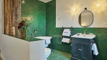 Une salle de bain avec un mur recouvert de carreaux verts, un mur d’accent en bois, un lavabo, des toilettes et un meuble-lavabo de couleur foncée.