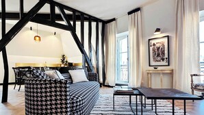 Een moderne woonkamer met zichtbare houten balken, een hondentandsofa, een eethoek en een open haard.