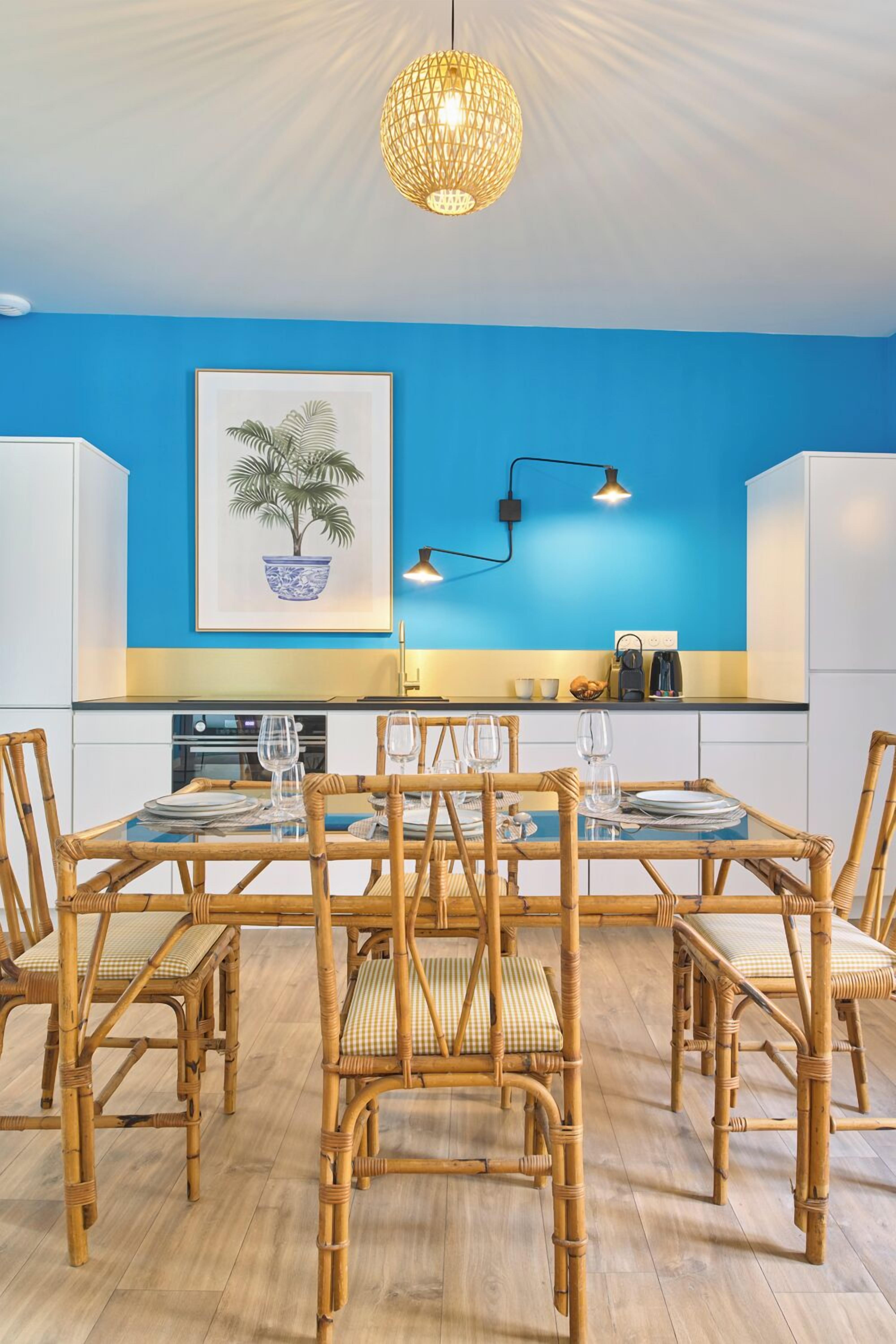 A dining area with a blue wall, a framed plant, and a hanging light fixture.