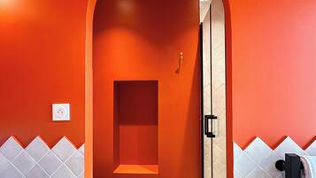 Et badeværelse med rød væg, hvid toilet og bruseområde.