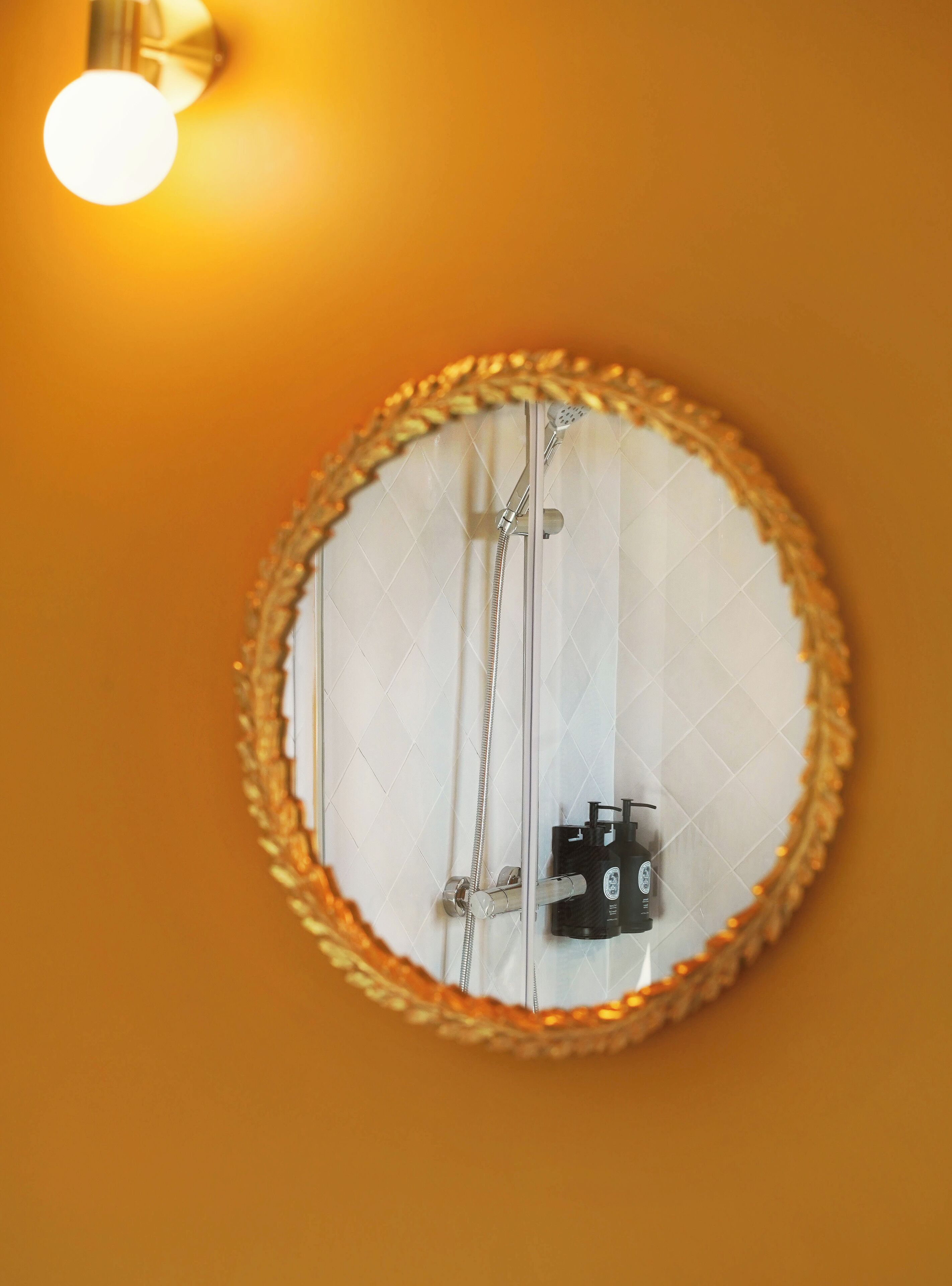 Un bagno con uno specchio rotondo, una doccia e un portalampada a parete.