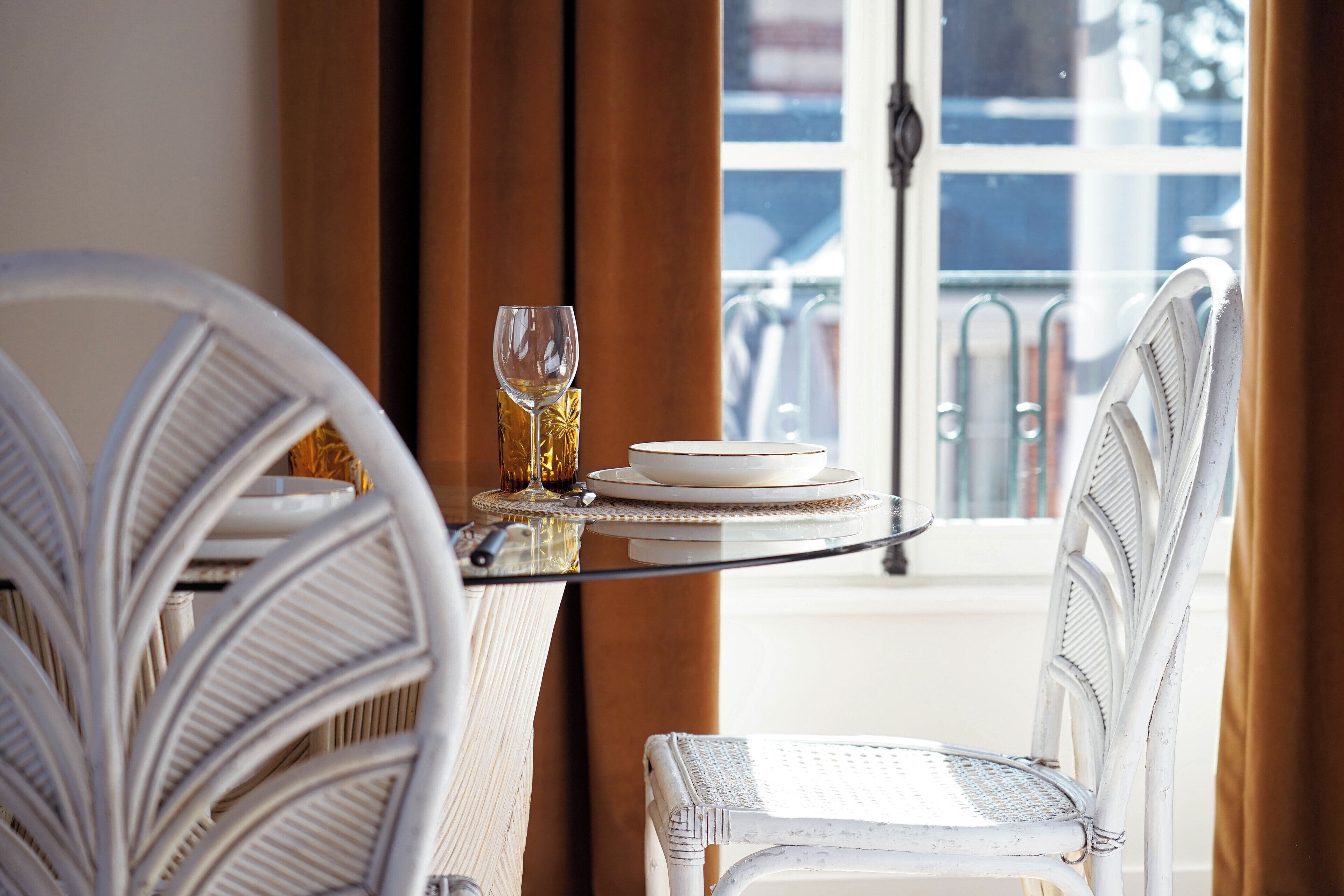 Un comedor con sillas de mimbre y una mesa de cristal, servida con platos y una copa de vino.