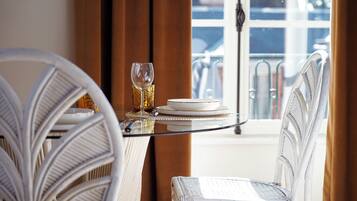 Un comedor con sillas de mimbre y una mesa de cristal, servida con platos y una copa de vino.