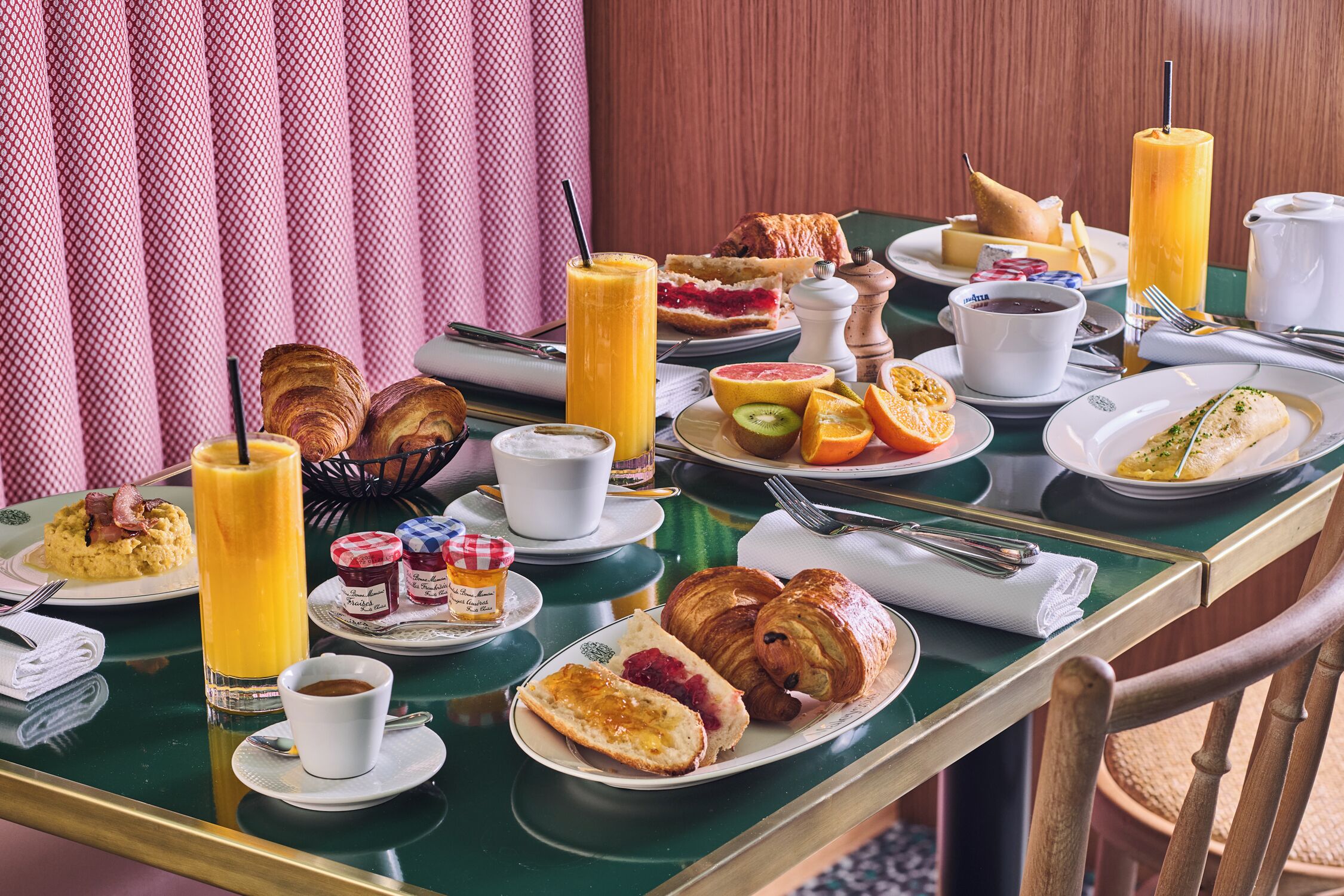 Une table de petit-déjeuner avec des croissants, des viennoiseries, des fruits et des boissons.