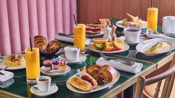 Une table de petit-déjeuner avec des croissants, des viennoiseries, des fruits et des boissons.