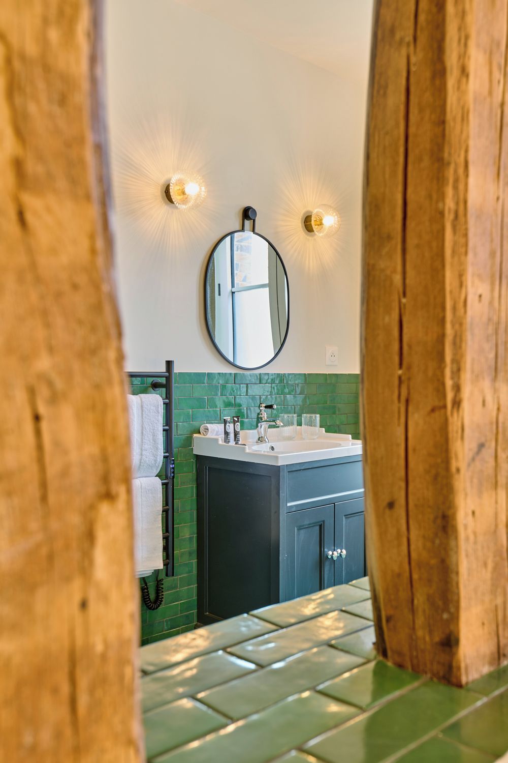 Un baño con piso de azulejos verdes, un lavamanos blanco, un espejo y dos luces empotradas.