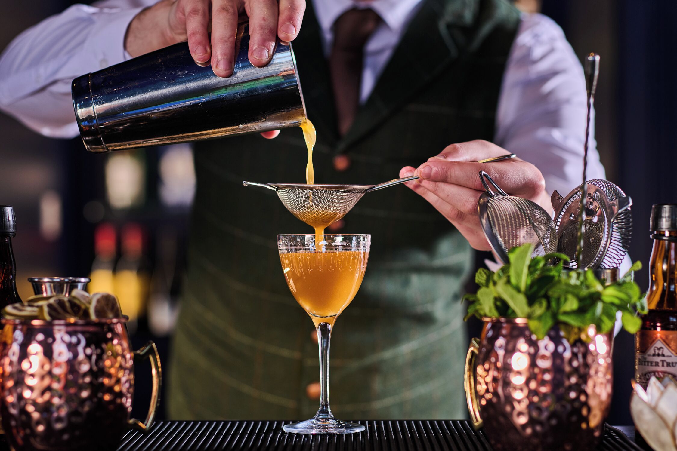 A bartender pouring a drink into a glass using a strainer.