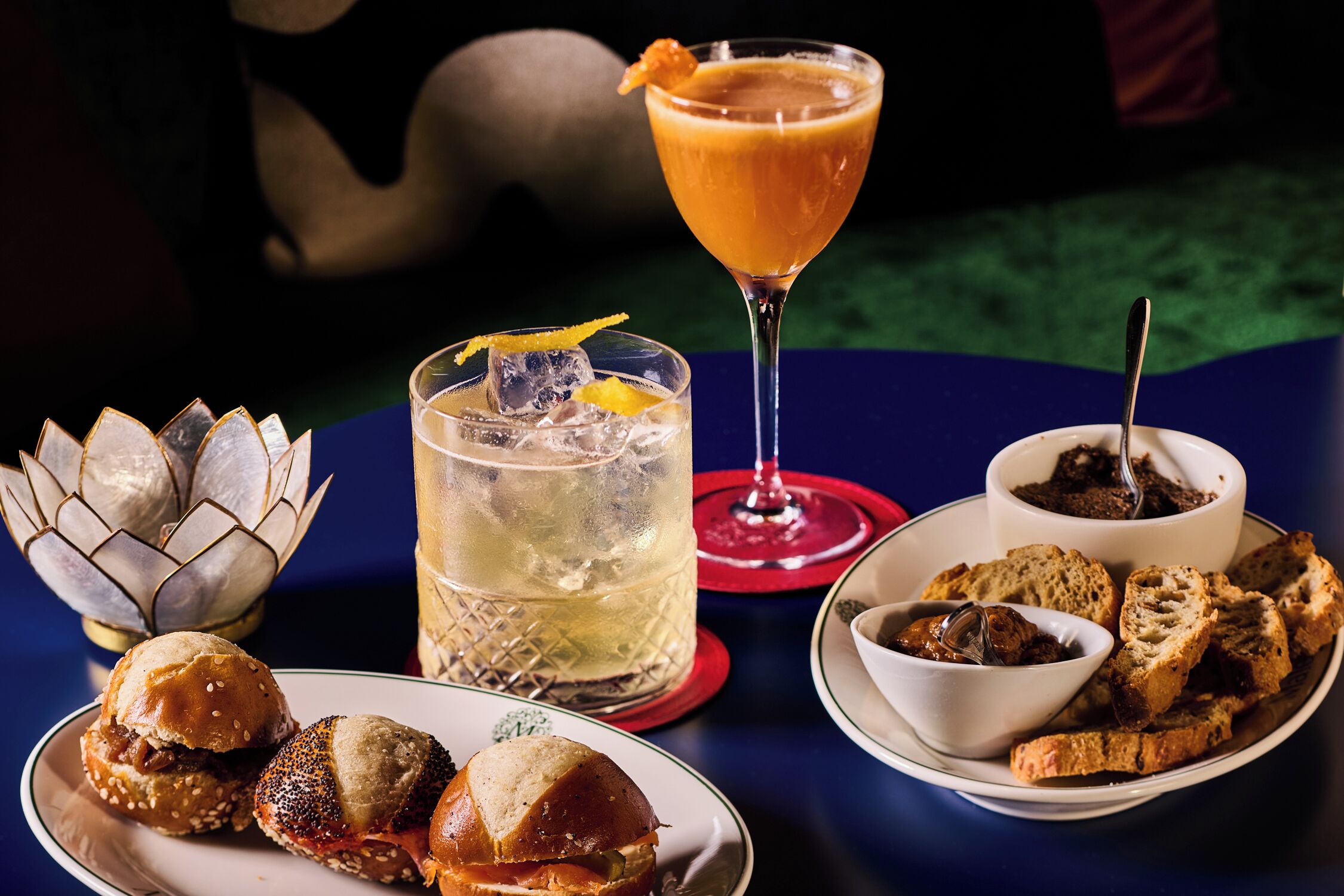 A table with food and drinks, including sandwiches, bread, and a cocktail.
