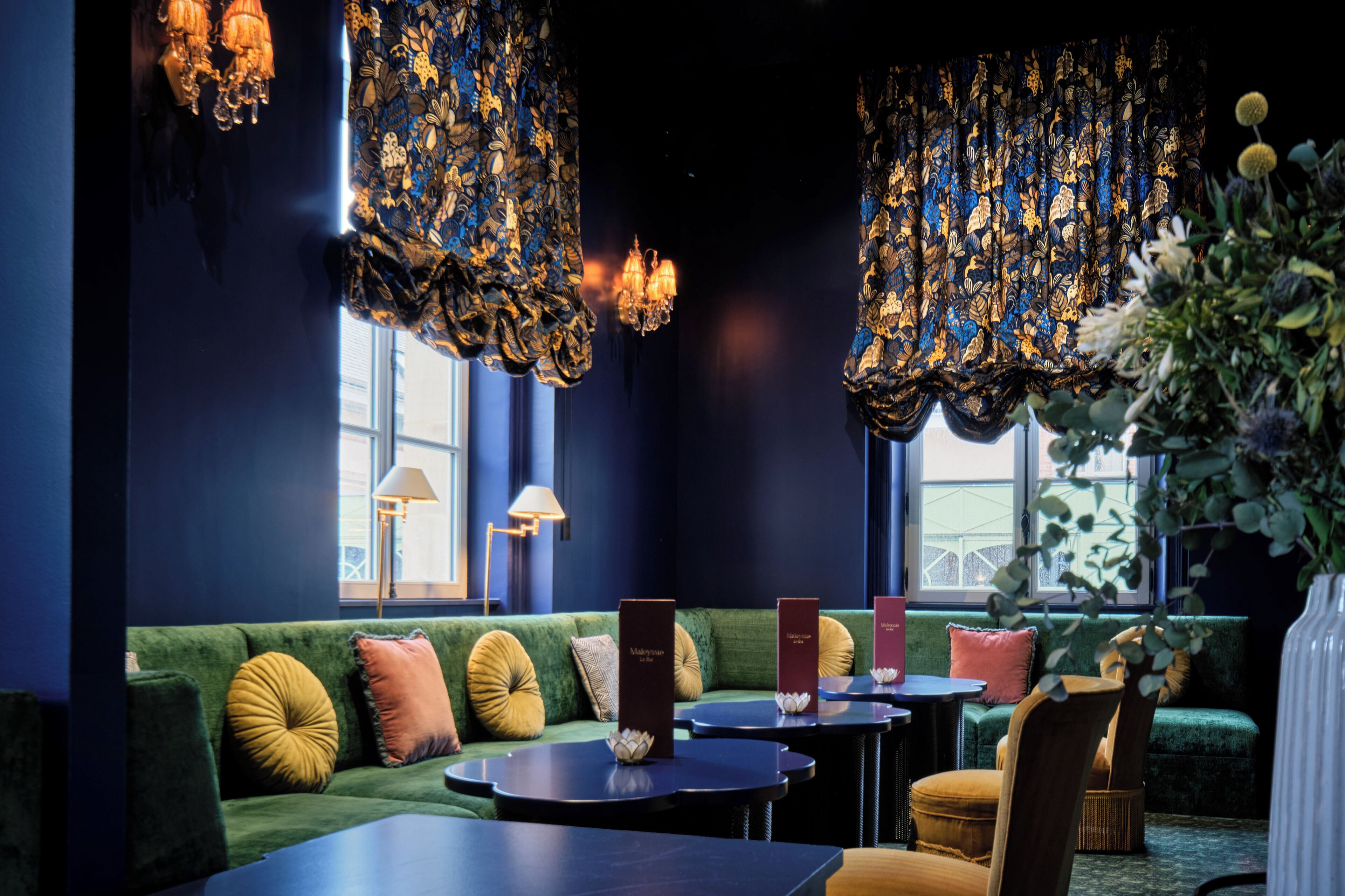 Een gezellige zithoek met een groene bank, ronde tafels en hangende decoraties.
