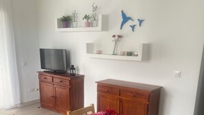 A dining area with a wooden table, chairs, a vase of flowers, a television on a cabinet, and decorative items on shelves. - APARTMENT IN CALA'N FORCAT (Los Delfines)