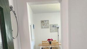A hallway leading to a dining area with a wooden table and chairs, a white wall with framed pictures, and a green door. - APARTMENT IN CALA'N FORCAT (Los Delfines)
