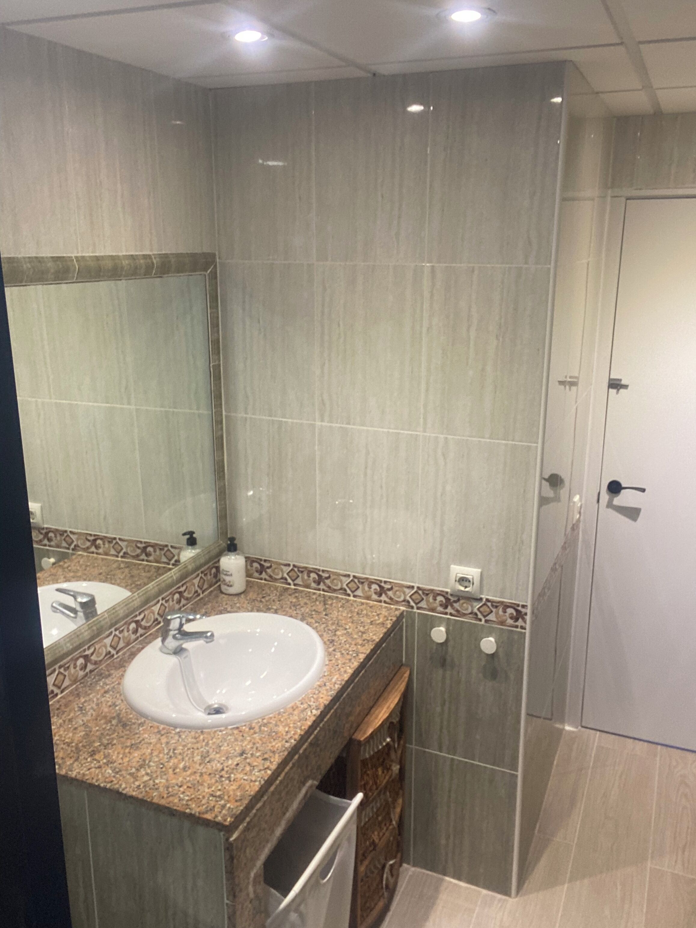 Une salle de bain moderne avec un lavabo surmonté d’un plan de travail en granit, un miroir et un espace douche.