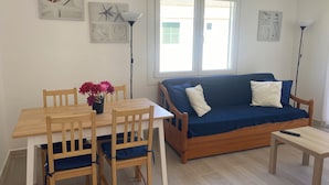 A cozy living area with a wooden table, blue cushioned chairs, a blue sofa with pillows, and a floor lamp. - APARTMENT IN CALA'N FORCAT (Los Delfines)