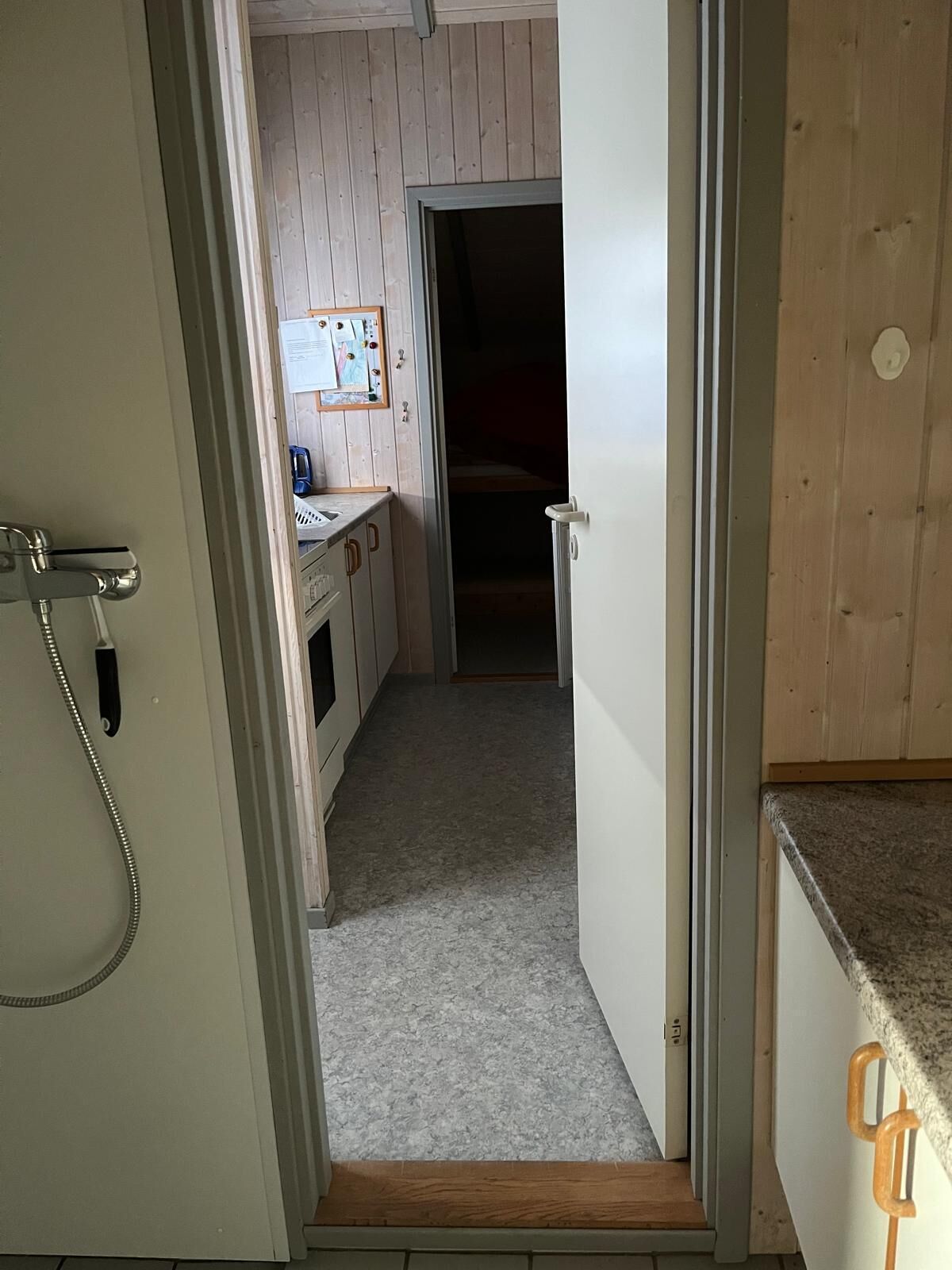 Een smalle gang die uitkomt in een keuken met houten kastjes en een aanrecht.