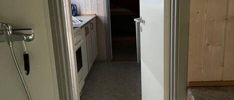 Een smalle gang die uitkomt in een keuken met houten kastjes en een aanrecht.