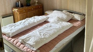 Ein Zimmer mit einem Einzelbett, einem Holzkopfende, einer Kommode mit Pflanze und einem Heizkörper.