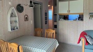 Ein gemütliches Zimmer mit Esstisch, Stühlen, einer Küchenzeile mit Schränken und einer Holzkονstruktion an der Decke.