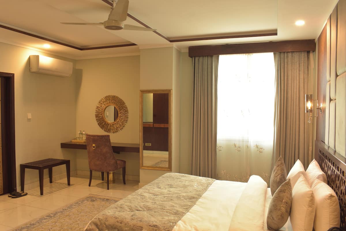 A hotel room with a bed, a desk, a chair, a mirror, and a ceiling fan.