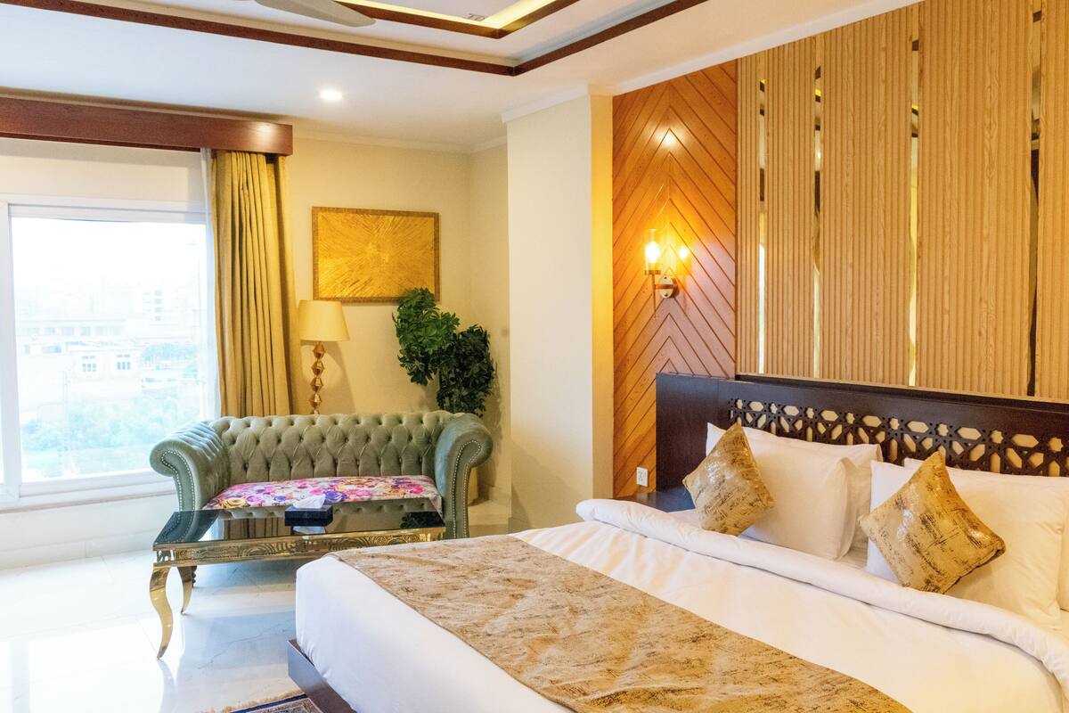 A hotel room with a large bed, a green armchair, a small table, and a wooden wall panel.