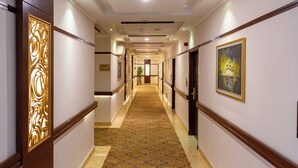 Un couloir d’hôtel avec un tapis à motifs, des lambris en bois et des œuvres d’art encadrées accrochées aux murs.