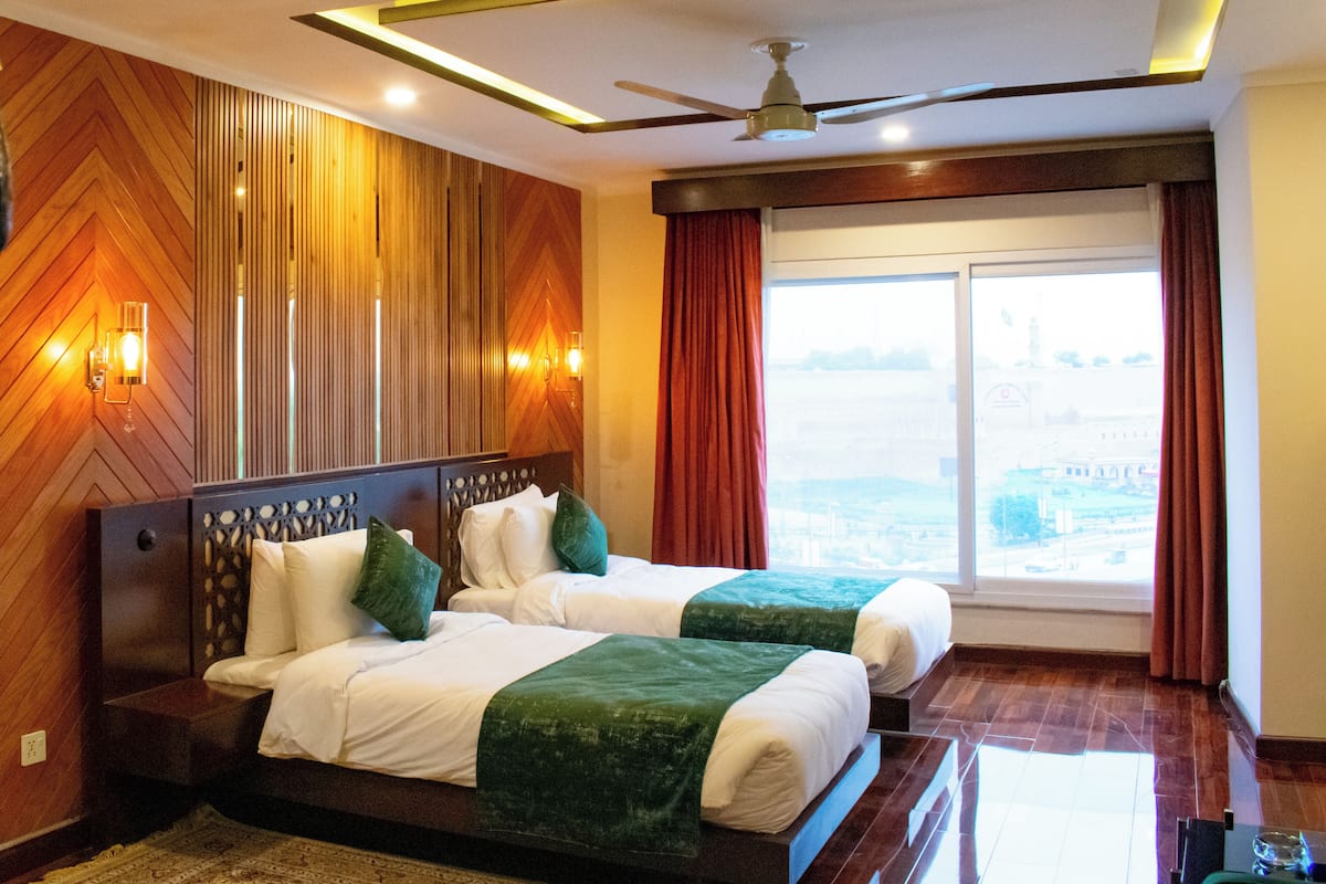 A hotel room with a large bed, two pillows, a ceiling fan, and a view of the city through the window.