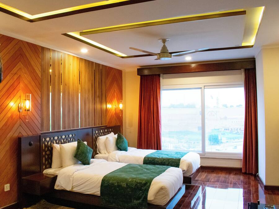 A hotel room with a large bed, two pillows, a ceiling fan, and a view of the city through the window.