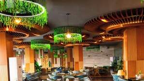 Un restaurant doté de nombreuses tables et chaises, avec un design moderne agrémenté de plantes vertes suspendues et de touches de bois.