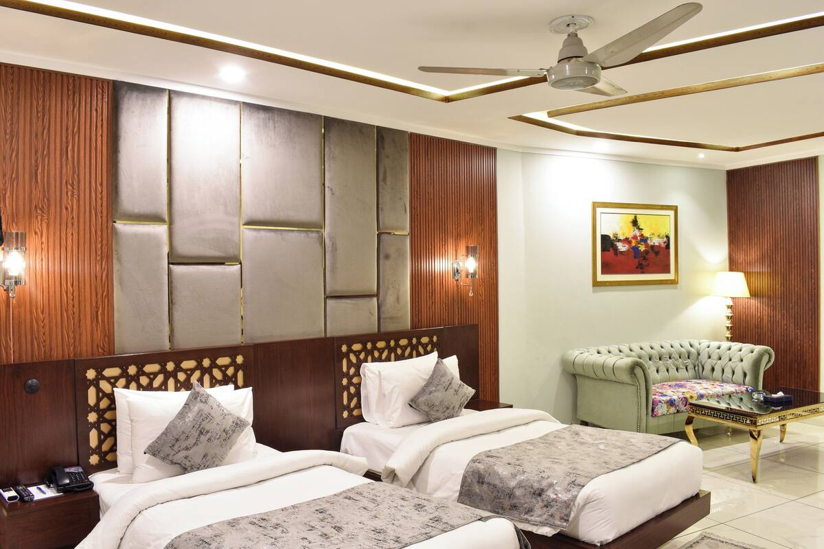 A hotel room with two beds, a green sofa, a ceiling fan, and a painting on the wall.