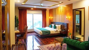 Une chambre d’hôtel moderne avec un grand lit, un bureau, un canapé vert et une vue sur l’extérieur.