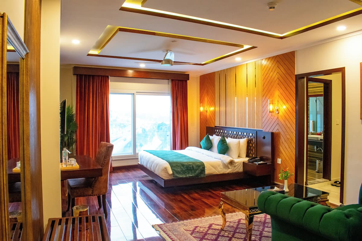 A modern hotel room with a large bed, a desk, a green sofa, and a view of the outdoors.