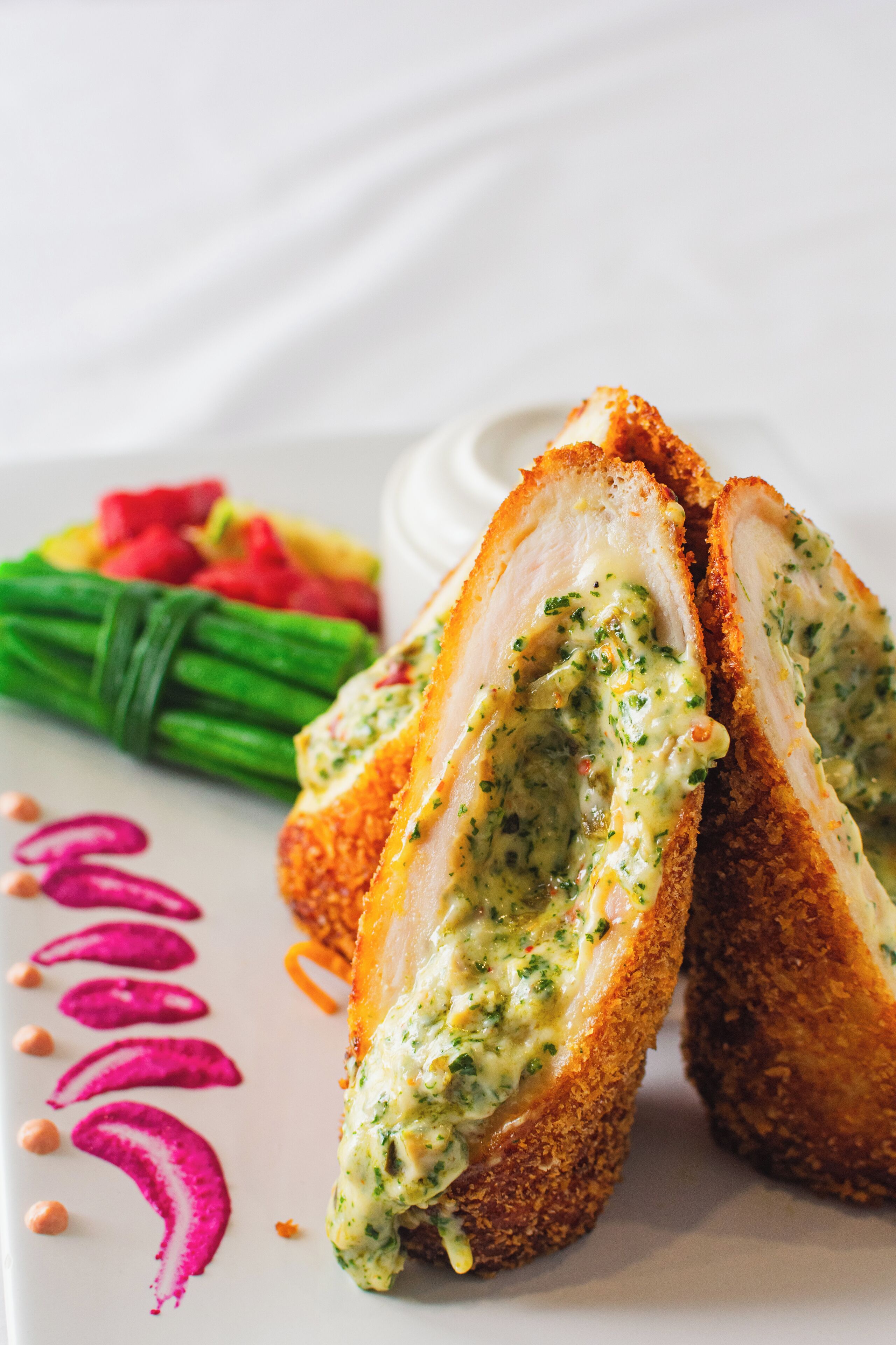 Un plato con pollo empanizado y salsa verde, acompañado de verduras y una salsa decorativa sobre un plato blanco.