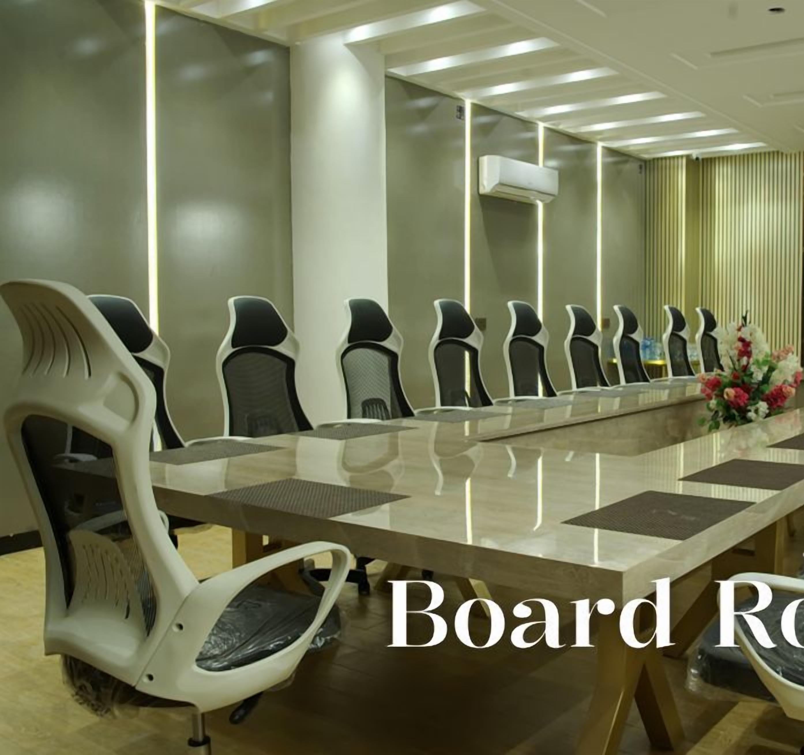 Uma sala de reuniões com uma mesa comprida e várias cadeiras, ar condicionado e um arranjo floral decorativo.