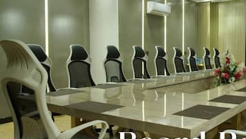 Uma sala de reuniões com uma mesa comprida e várias cadeiras, ar condicionado e um arranjo floral decorativo.