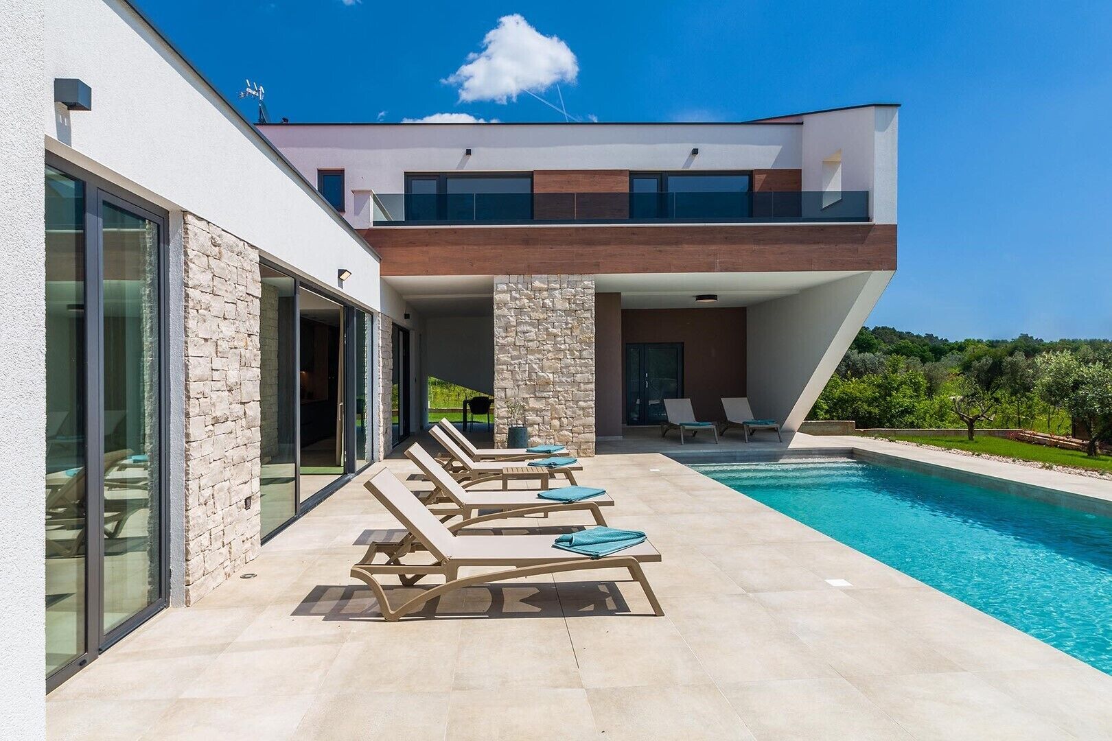 A modern two-story house with a swimming pool, stone pillars, and lounge chairs.