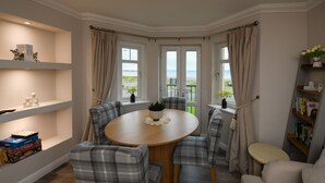 A dining area with a round table, plaid chairs, a bookshelf, and a view of the outdoors. - Barassie Bay View apartment (Troon)