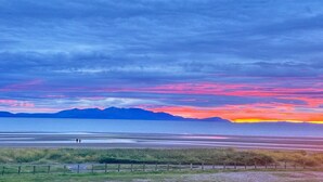 A coastal landscape with a flat terrain, a fence, and distant mountains under a colorful sky. - Barassie Bay View apartment (Troon)