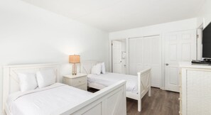 A bedroom with two single beds, a bedside table with a lamp, a wardrobe, and a television on a stand. - Ferris Wheels, Bay Thrills & Sunset Chills | OCMD Bayfront Fun (Ocean City)