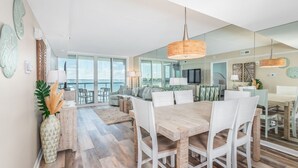 A spacious living area with a large dining table, white chairs, and a view of the ocean through large windows. - Crab Feasts, Bay Breezes & Boardwalk Nights | Summer Starts Here (Ocean City)
