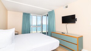 Habitación de hotel con cama, televisión montada en la pared y vista al mar a través de un ventanal grande.