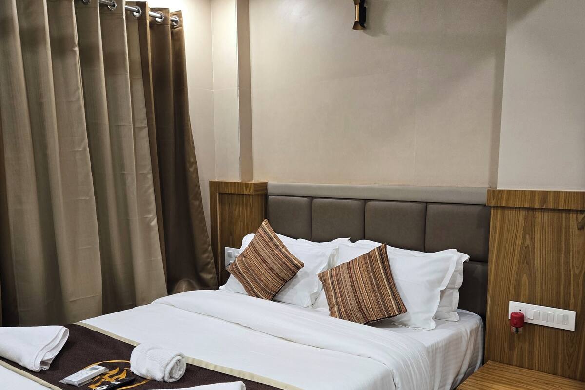 A neatly made bed with white and brown bedding, a wooden headboard, and a bedside table with a red switch.