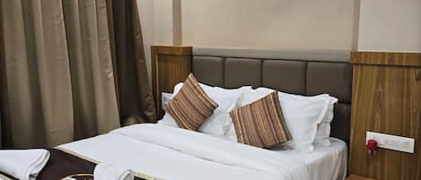 Una cama bien hecha con ropa de cama blanca y marrón, un cabecero de madera y una mesita de noche con un interruptor rojo.
