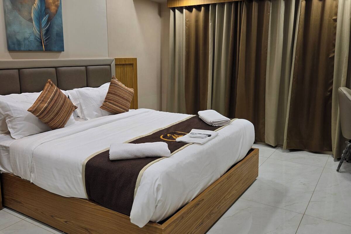 A modern hotel room with a large bed, a ceiling fan, an air conditioning unit, and a painting on the wall.