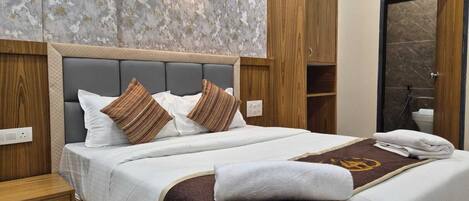 Une chambre d’hôtel avec un grand lit, une tête de lit en bois et une douche carrelée en marbre.