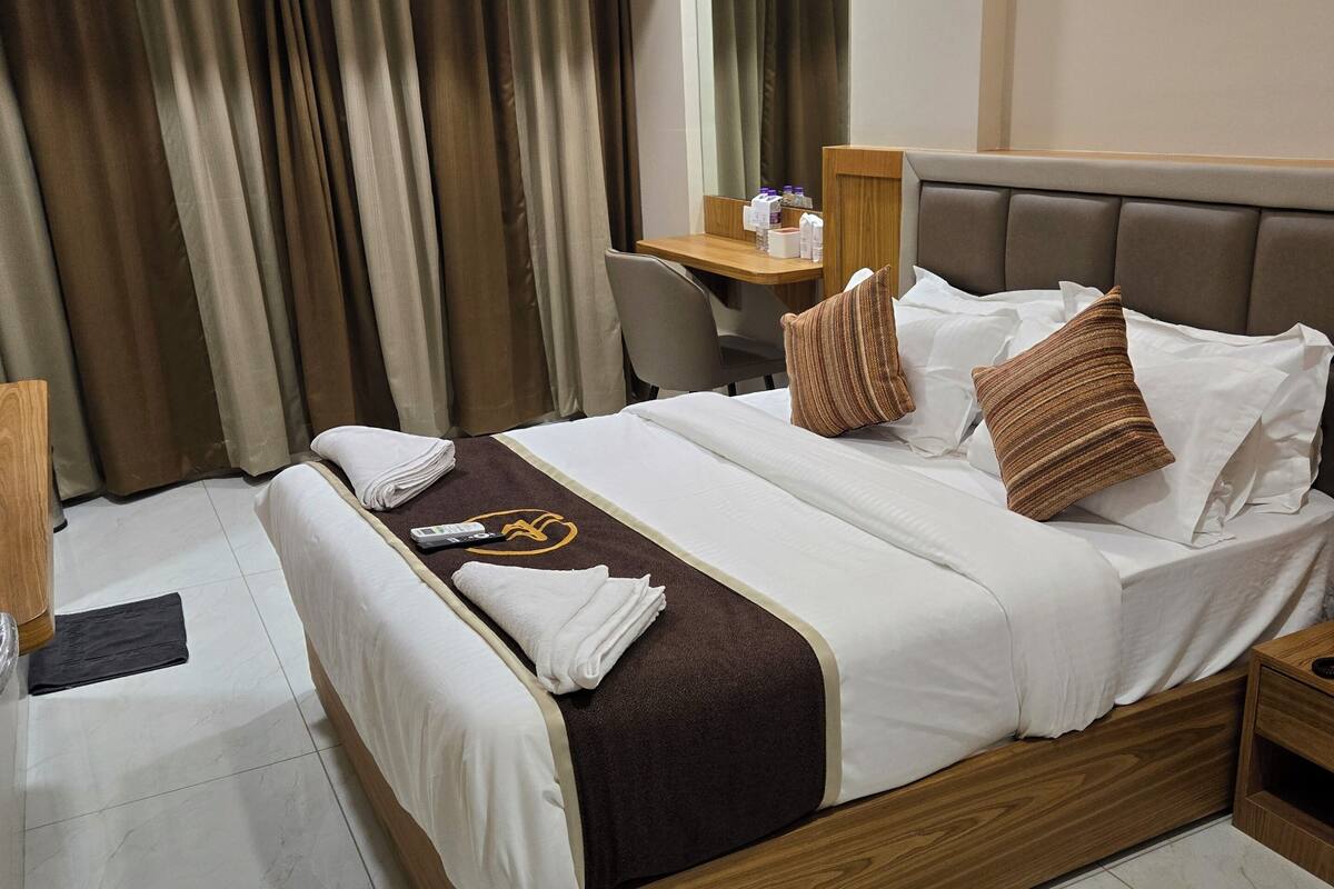 A hotel room with a bed, a desk, a chair, an air conditioner, and a mirror.