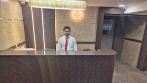 Una reception con un uomo dietro, una telecamera di sicurezza sopra e un cartello che indica l'accessibilità per disabili al muro.