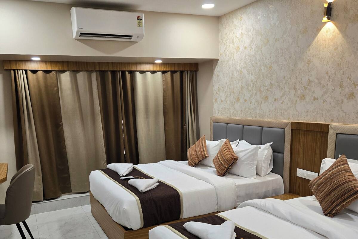 A hotel room with two beds, a desk, an air conditioner, and a ceiling fan.