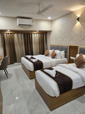 A hotel room with two beds, a desk, an air conditioner, and a ceiling fan.