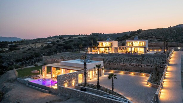 A modern villa with a swimming pool, stone walls, and a view of the surrounding landscape.